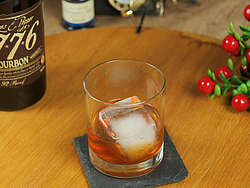 Der Cocktail Old Fashioned im Tumbler mit einem Eiswürfel, eine Flasche Whisky 1776 und Deko